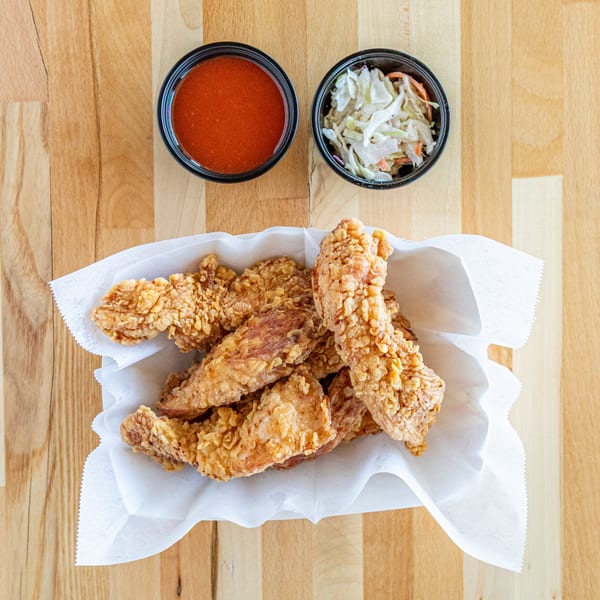 Crispy fried chicken tenders in a paper-lined basket with sides of hot sauce and coleslaw.