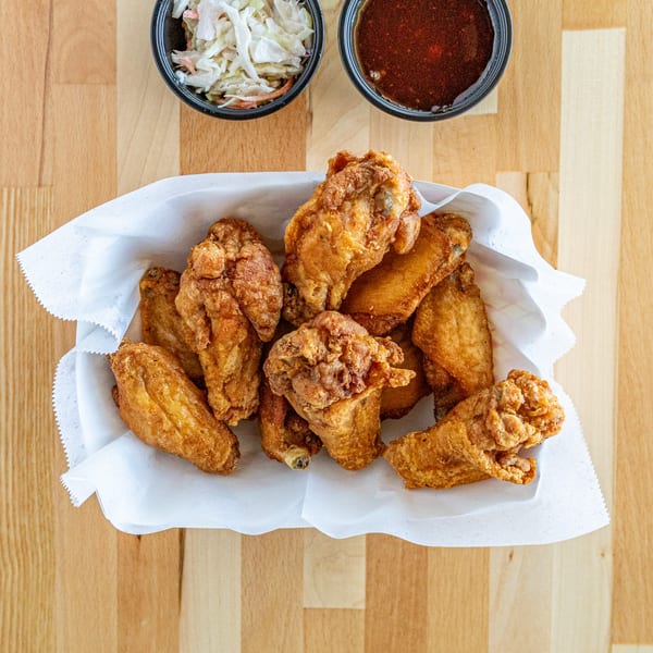 Crispy fried chicken wings in a white paper-lined basket with coleslaw and dipping sauce.