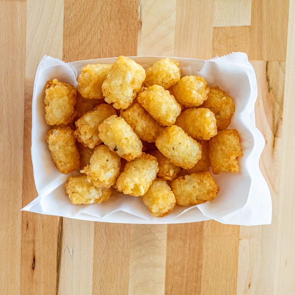 A white paper tray filled with golden-brown, crispy tater tots on a light wooden surface.