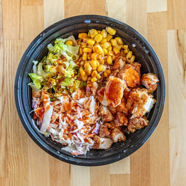 Wings to Us fried chicken bowl with corn, coleslaw, and lettuce on a wooden table.