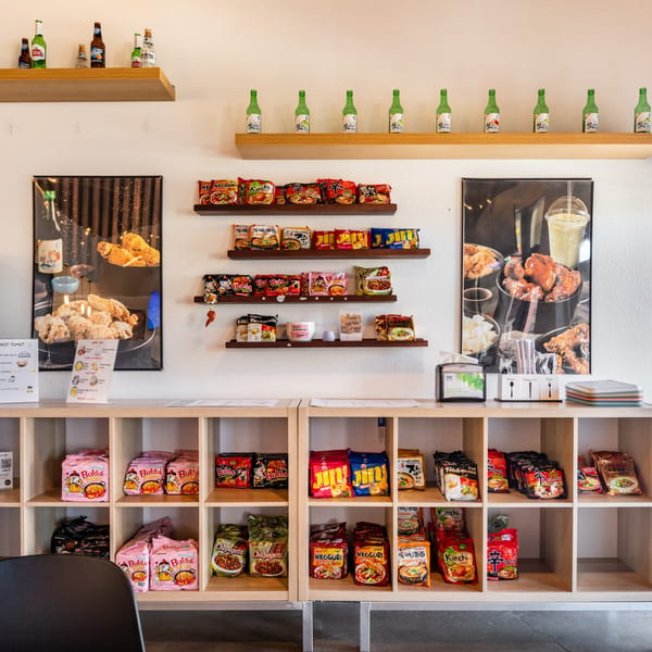 A wall display at Wings to Us with instant ramen, beer bottles, and fried chicken posters.