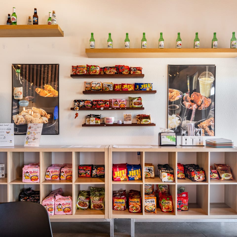A wall display at Wings to Us with instant ramen, beer bottles, and fried chicken posters.