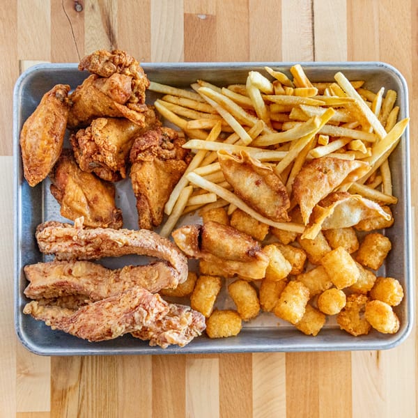 A metal tray filled with fried chicken wings, tenders, french fries, tater tots, and fried wontons.