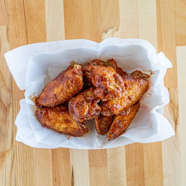 A white paper-lined basket filled with glossy, sauced fried chicken wings on a wooden table.