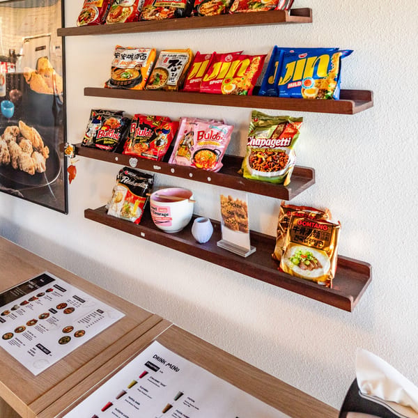 A wall display of various instant ramen packages above a wooden counter with menus.